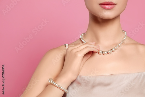 Young woman wearing elegant pearl jewelry on pink background, closeup. Space for text