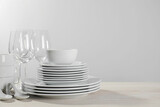 Set of clean dishware and glasses on white wooden table against light background. Space for text