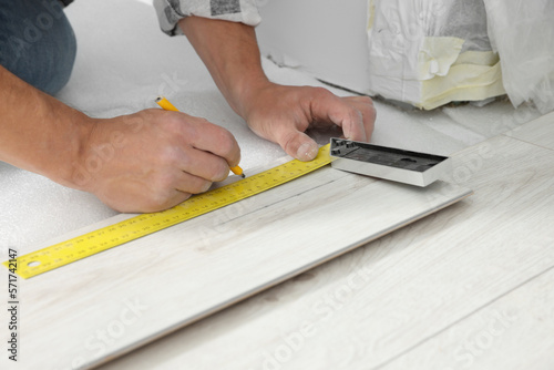 Professional worker using measuring tape and pen during installation of laminate flooring, closeup