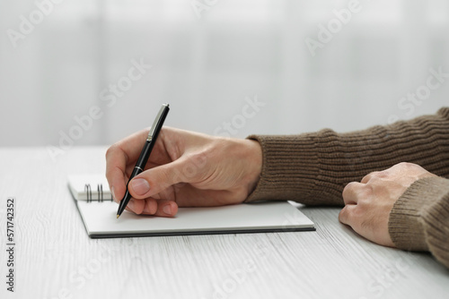 Man writing in notebook at white wooden table, closeup