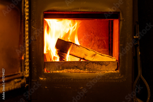 Close up of wooden logs burning in wood burning fire with open door in home living room.