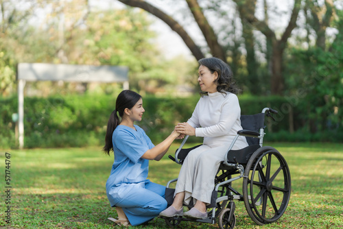 Young asian care helper with asia elderly woman on wheelchair relax together park outdoors to help and encourage and rest your mind with green nature. hold hands to encourage