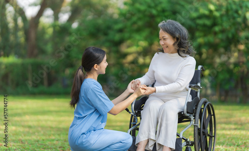 Young asian care helper with asia elderly woman on wheelchair relax together park outdoors to help and encourage and rest your mind with green nature. hold hands to encourage © NanSan