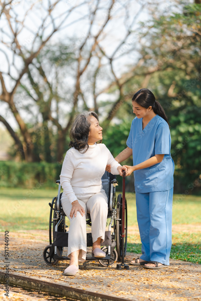 Young asian care helper with asia elderly woman on wheelchair relax together park outdoors to help and encourage and rest your mind with green nature. Young asian care helper with asia elderly woman on wheelchair relax together park outdoors to help and encourage and rest your mind with green nature.