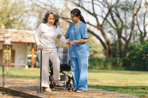 Young asian care helper with asia elderly woman on wheelchair relax together park outdoors to help and encourage and rest your mind. using crutches and cane help support yourself to walk