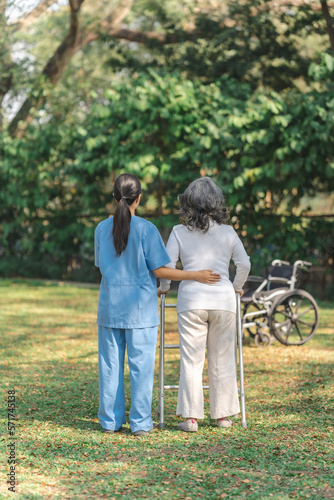 Young asian care helper with asia elderly woman on wheelchair relax together park outdoors to help and encourage and rest your mind with green nature. Help support yourself to learn to walk. walker
