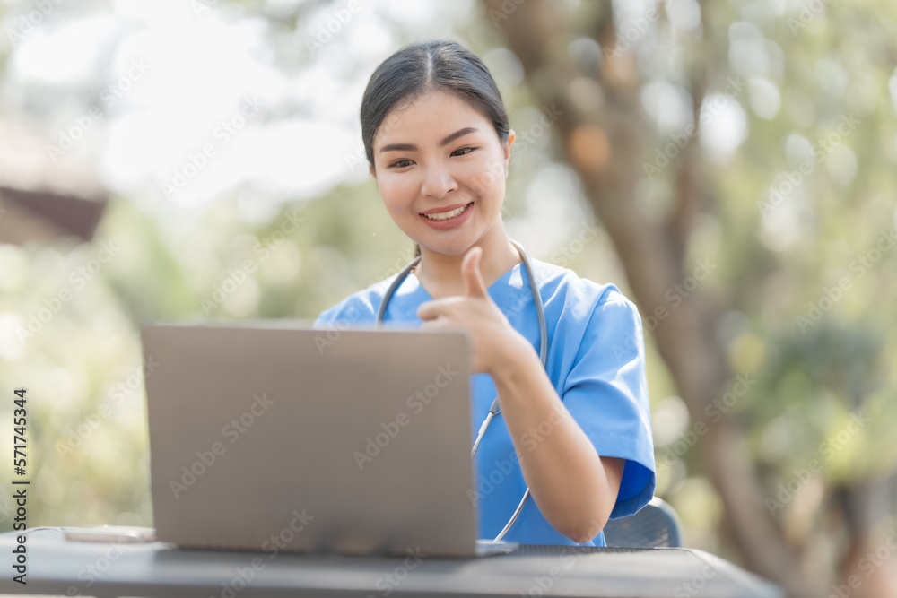 Asian female nurse working outdoor video call with patient online on laptop at desk in park.
