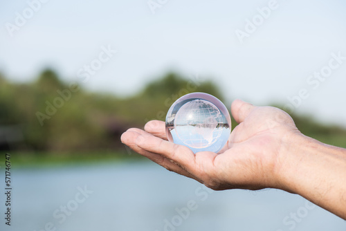 Crystal globe in male hand and on river background.