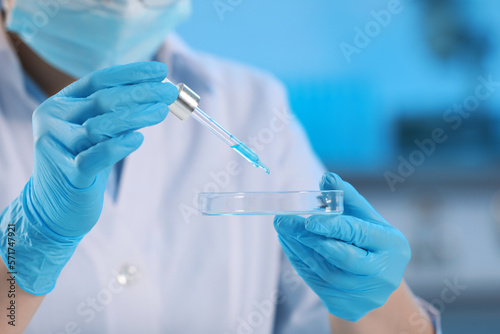 Scientist dripping liquid from pipette into petri dish in laboratory  closeup