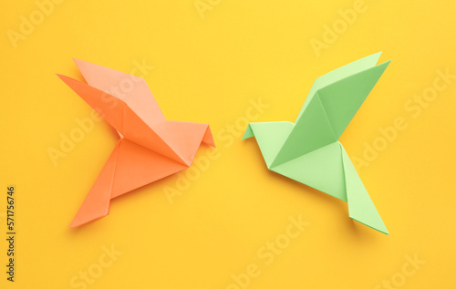 Origami art. Colorful handmade paper birds on yellow background, flat lay © New Africa