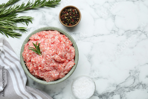 Bowl of raw fresh minced meat with rosemary and spices on white marble table, flat lay. Space for text