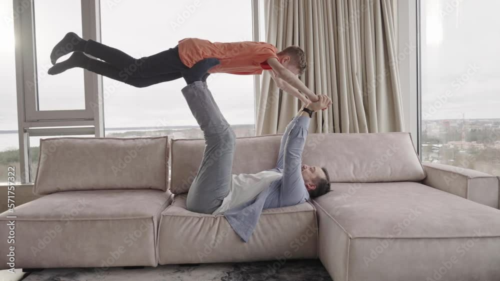 Father and son having fun at home. Parents spending quality time with children's. Joyful father lying on sofa and lifting excited happy son. Father and son having fun at home. Parents spending quality time with children's. Joyful father lying on sofa and lifting excited happy son.