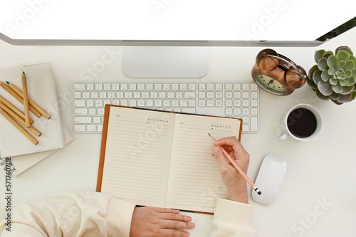 Top view of a modern workspace with a female's hand writing something on her notebook or diary