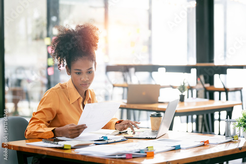 Young ethnic businesswoman looking seriously working on laptop computer and document at her desk office.