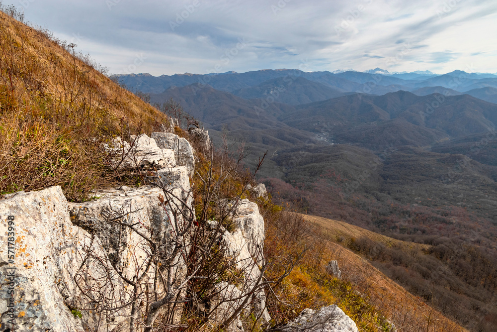 Large stones on the slope of a high mountain. View of the mountain range under a cloudy sky. Panoramic view of the Caucasus mountains. Dry grass on the slope of a high mountain. Mountain landscape.