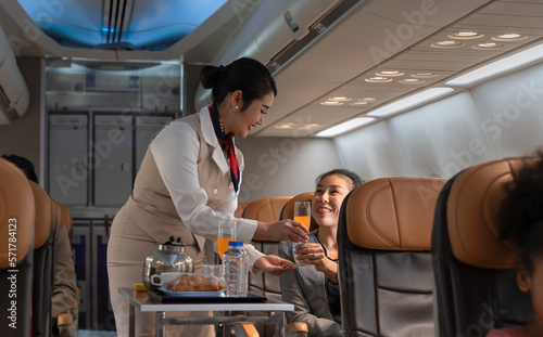 Airplane flight attendant serving orange juice to female passenger in cabin.