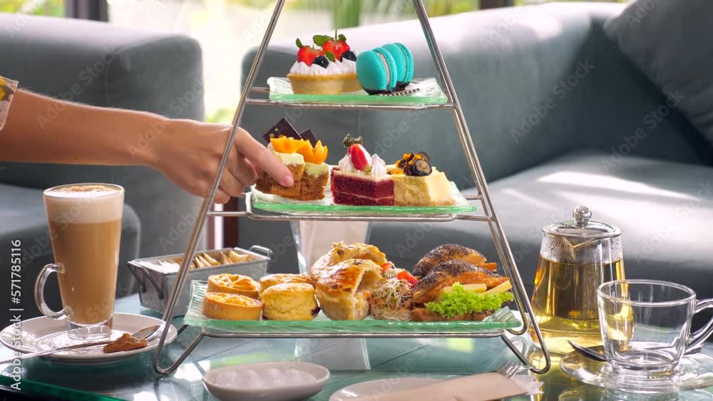 Woman hand take slice of cake from a towering display of afternoon tea Woman hand take slice of cake from a towering display of afternoon tea