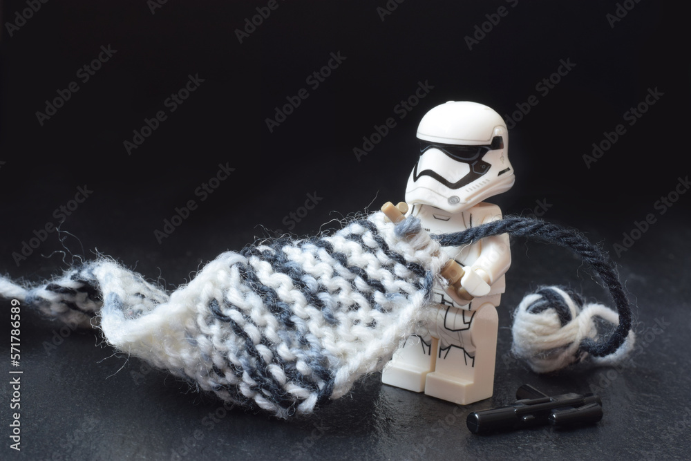 Naklejka premium Lego minifigure of warrior Star Wars is knitting a long scarf with stocks. Editorial illustrative image of popular plastic constructor. Stop war concept image.