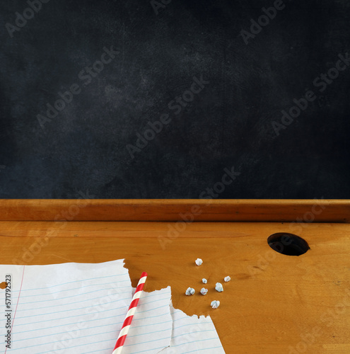 Spitballs, with red and white striped straw and paper on a vintage school desk top with copyspace on the blackboard