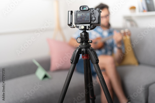 Man sitting in a living room, recording a video for a blog with a camera on a tripod.