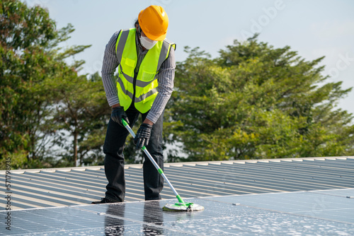 Maintenance technician using cleaning mop and to clean the solar panels that are dirty with dust to improve the efficiency of solar energy storage.