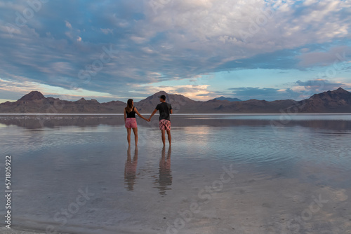 Silhouette of loving couple walking after sunrise on salt lake of Bonneville Salt Flats, Wendover, Western Utah, USA, America. Beautiful water reflections. Dreamy landscape with romantic atmosphere