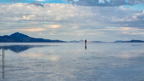 Man sillhoutte walking into sunset of lake Bonneville Salt Flats, Wendover, Western Utah, USA, America. Beautiful summits of Silver Island Mountain range reflecting in water surface, Great Salt Lake