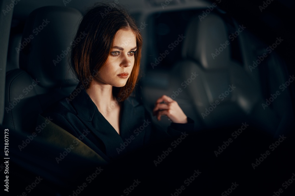 a close horizontal portrait of a stylish, luxurious woman in a leather coat sitting in a black car at night in the passenger seat