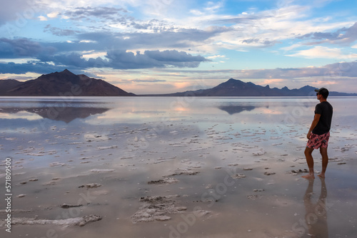 Man sillhoutte walking into sunset of lake Bonneville Salt Flats  Wendover  Western Utah  USA  America. Beautiful summits of Silver Island Mountain range reflecting in water surface  Great Salt Lake