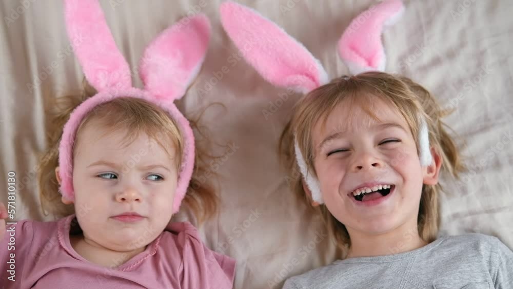 Happy cheerful children, baby girl and boy, wearing bunny ears headband lying on soft blanket, smiling and laughing. Siblings Enjoying the holidays. Easter day. Christian Passover. Celebrating Easter Happy cheerful children, baby girl and boy, wearing bunny ears headband lying on soft blanket, smiling and laughing. Siblings Enjoying the holidays. Easter day. Christian Passover. Celebrating Easter