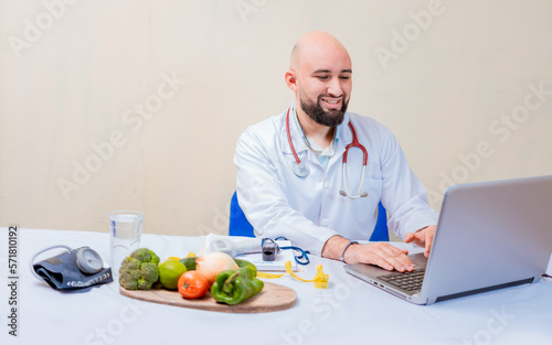 Nutritionist doctor using laptop at workplace. Bearded nutritionist doctor working on laptop at desk  Smiling nutritionist with laptop at desk