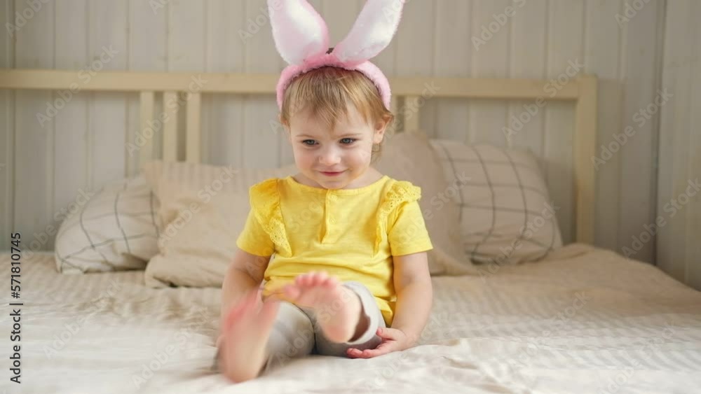 Baby girl with bunny ears. Cute funny baby play Easter eggs at home. Child playing colorful eggs indoors. Spring. Little kid celebrating Easter with traditional symbol of holiday and religion concept Baby girl with bunny ears. Cute funny baby play Easter eggs at home. Child playing colorful eggs indoors. Spring. Little kid celebrating Easter with traditional symbol of holiday and religion concept