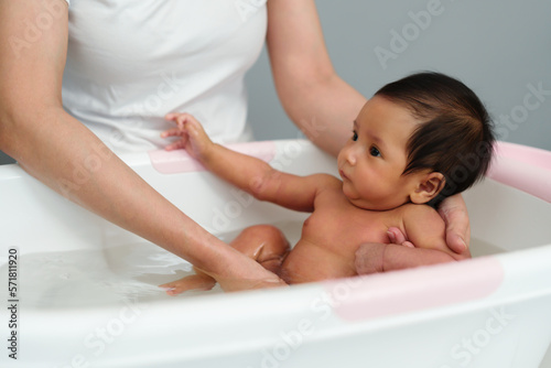 mother give a bath newborn baby in bathtub