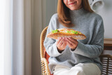 Closeup image of a young woman holding a piece of french baguette sandwich at home