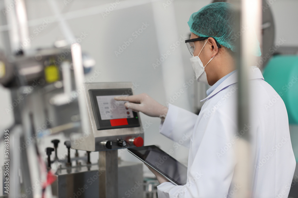 Worker man in personal protective equipment or PPE inspecting quality of mask and medical face mask production line in factory, manufacturing industry and factory concept. Worker man in personal protective equipment or PPE inspecting quality of mask and medical face mask production line in factory, manufacturing industry and factory concept.