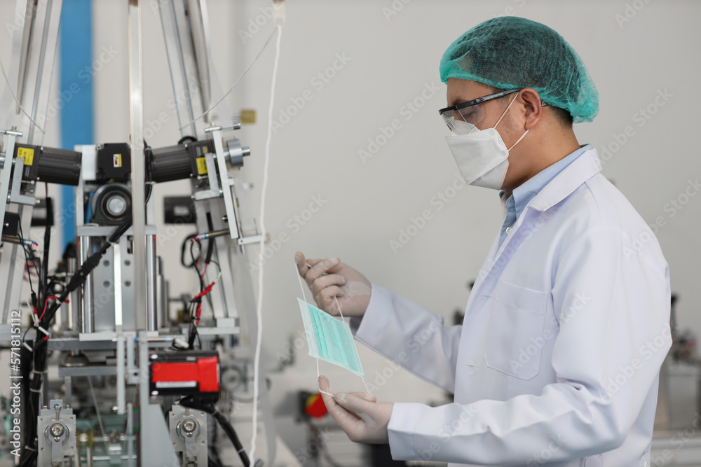 Worker man in personal protective equipment or PPE inspecting quality of mask and medical face mask production line in factory, manufacturing industry and factory concept. Worker man in personal protective equipment or PPE inspecting quality of mask and medical face mask production line in factory, manufacturing industry and factory concept.