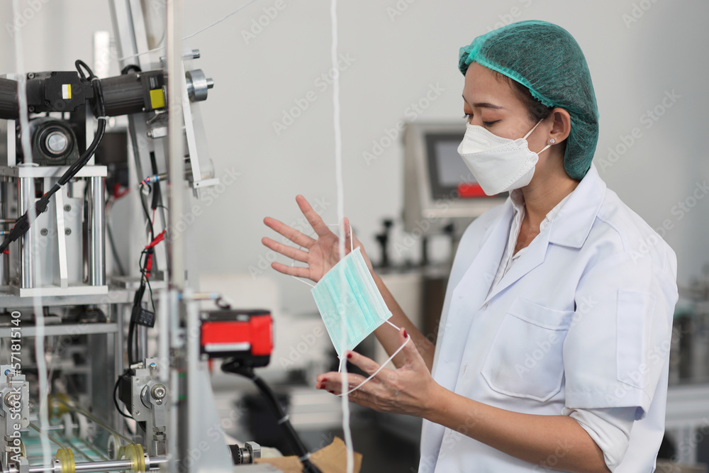 Worker woman in personal protective equipment or PPE inspecting quality of mask and medical face mask production line in factory, manufacturing industry and factory concept. Worker woman in personal protective equipment or PPE inspecting quality of mask and medical face mask production line in factory, manufacturing industry and factory concept.