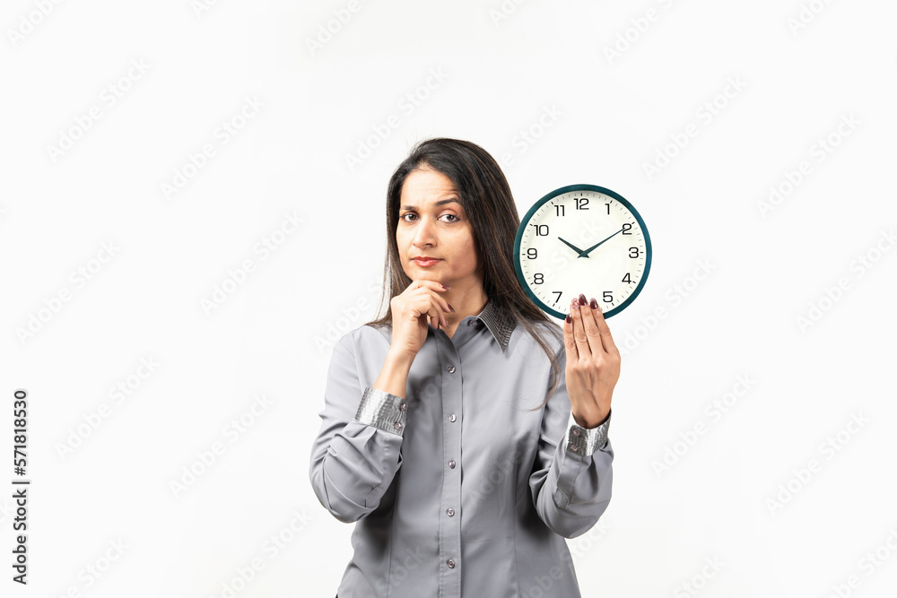 Mid aged Indian woman holding a clock isolated on white, confused, feels doubtful and unsure. Mid aged Indian woman holding a clock isolated on white, confused, feels doubtful and unsure.