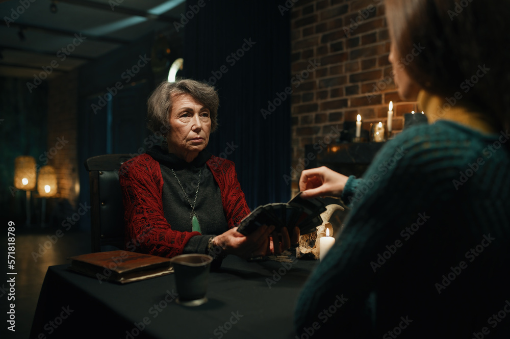 Old mature soothsayer holding divination tarot cards in front of client