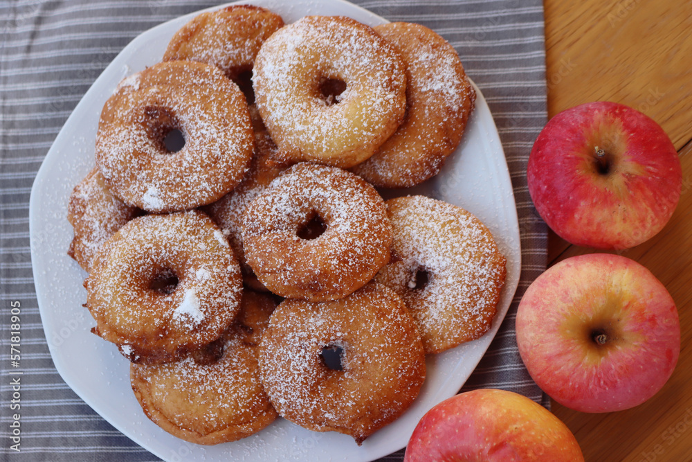 Homemade deep fried apple rings with batter sprinkled with powdered sugar ona white plate on wooden table with fresh apples Homemade deep fried apple rings with batter sprinkled with powdered sugar ona white plate on wooden table with fresh apples