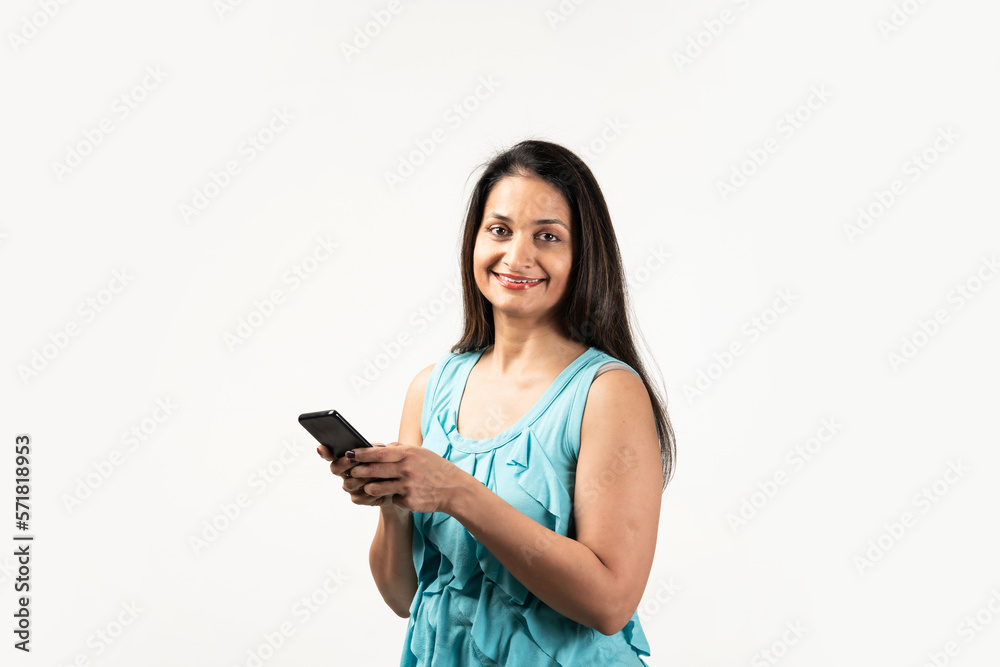 Portrait of a smiling Mid aged Indian woman holding smartphone over white background Portrait of a smiling Mid aged Indian woman holding smartphone over white background