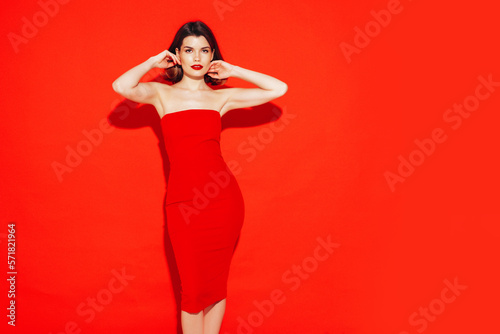 Portrait of young beautiful smiling female in trendy summer red evening dress. Sexy carefree brunette woman posing in studio, isolated. Positive model with evening makeup. Cheerful and happy