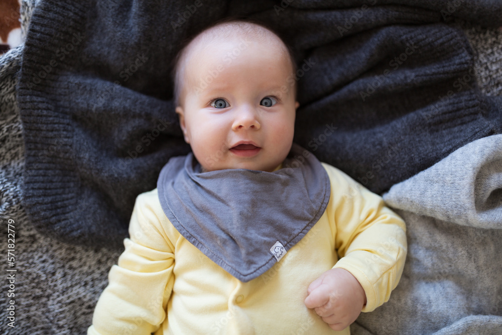 Happy caucasian baby girl five months old lying on knitted blanket. Colors of the year 2021 ultimate gray and illuminating Happy caucasian baby girl five months old lying on knitted blanket. Colors of the year 2021 ultimate gray and illuminating
