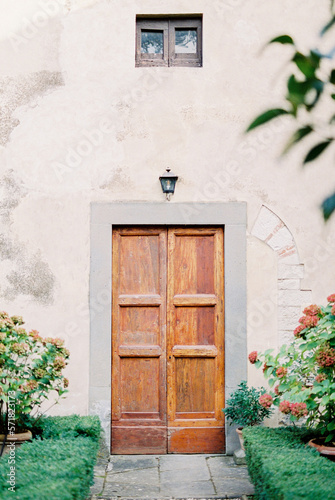 Wooden door in the stone wall of an old villa among green flowering bushes