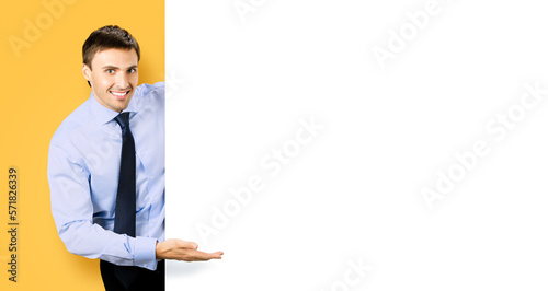 Portrait picture of young business man bank manager in confident cloth, necktie stand behind show empty white banner signboard billboard with copy space text area. Isolated on orange yellow background