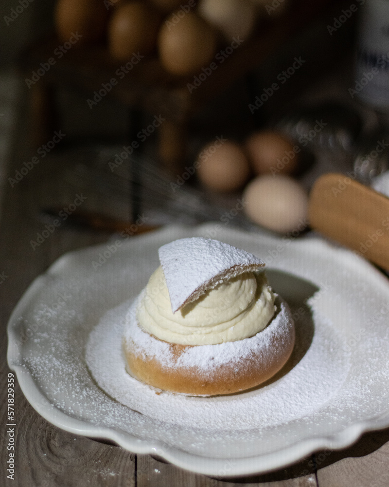 A Semla on a white porcelain plate with a lot of icing sugar at the top