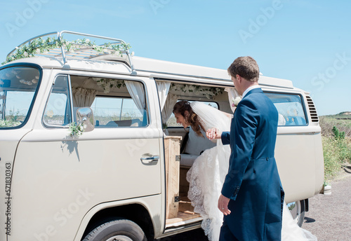 groom helping bride get into a camper van on their wedding day