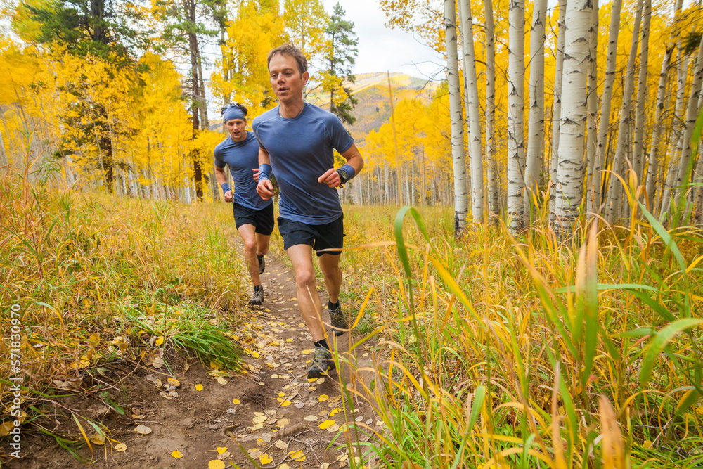 Men trail run through aspen forest with fall color in Vail, Colorado Men trail run through aspen forest with fall color in Vail, Colorado