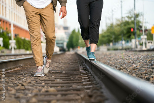 Young couple walking on train tracks in a city from the waist down