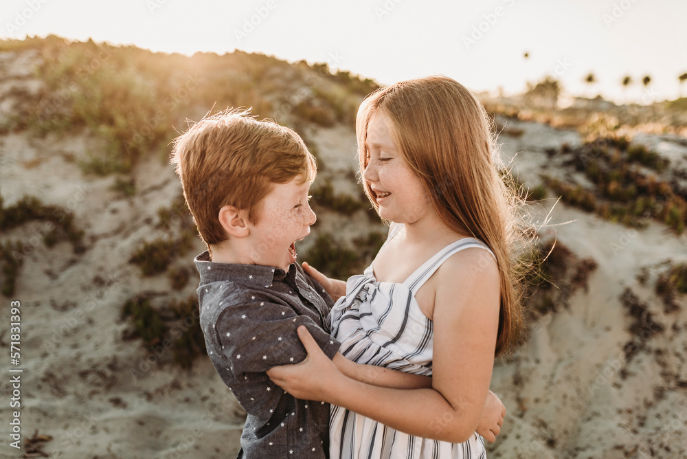 Side view of young brother and sister hugging and laughing at beach